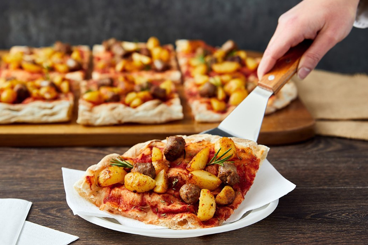 trancio di pinsa romana servita al ristorante con la quale si possono ottimizzare i costi di gestione comprando la base pinsa romana precotta di pinsami, condita con patate, salsiccia e rosmarino